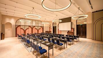 A conference room with multiple tables and chairs, large circular chandeliers, and a patterned carpet.