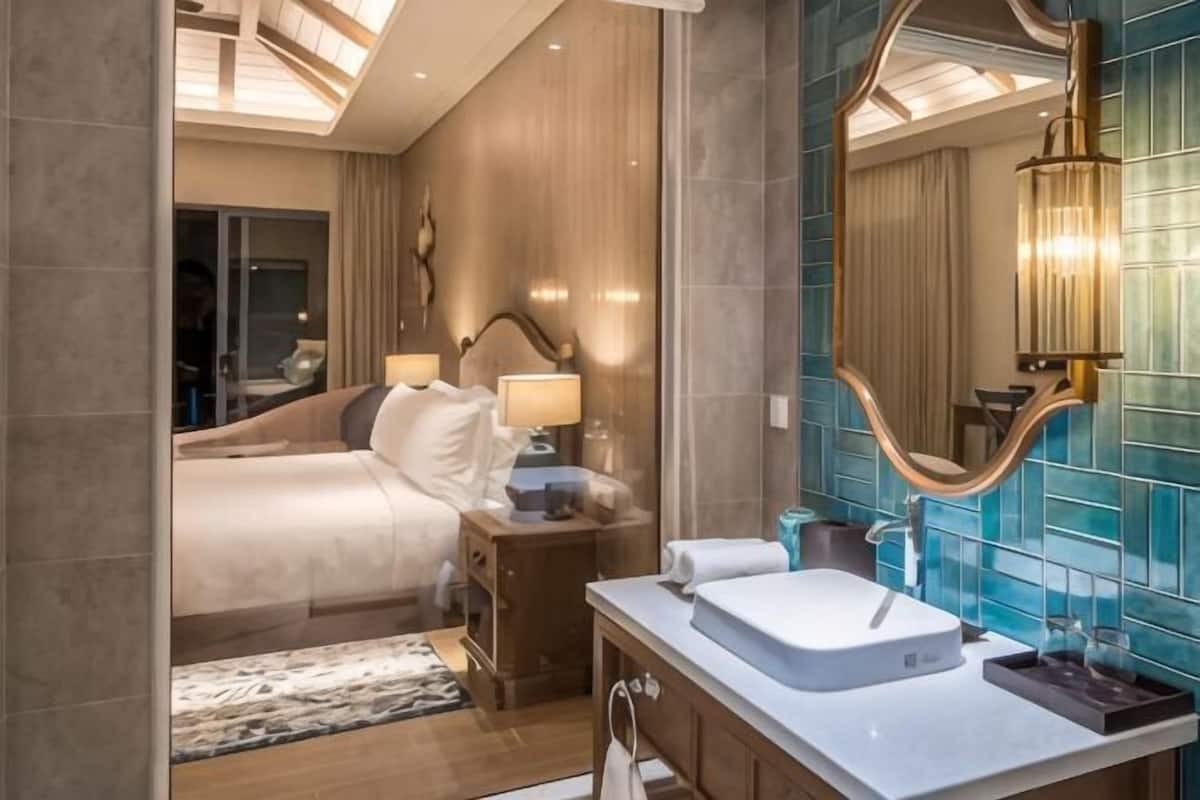 A modern hotel room with a large bed, bedside lamps, a vanity with a mirror, and a ceiling light fixture.