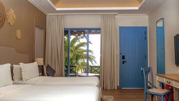 A hotel room with two beds, a balcony with curtains, a blue door, and a desk with a chair.