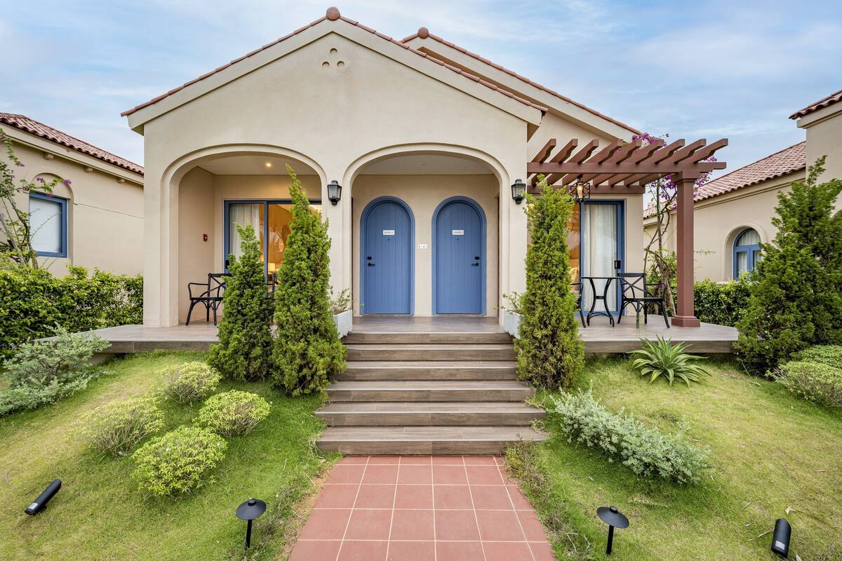 A two-story building with a beige facade, blue doors, and a covered porch with chairs.