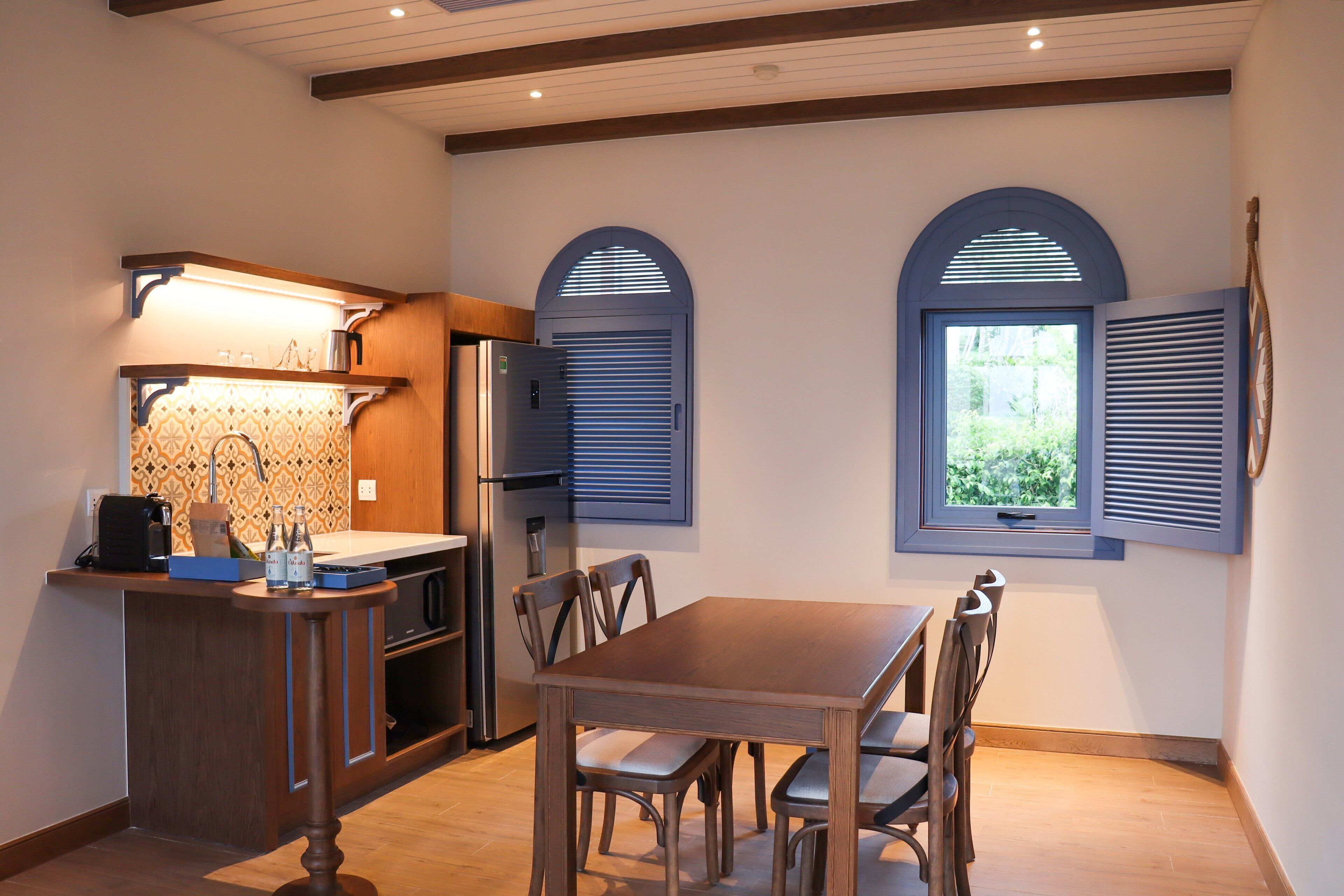 A compact kitchen with a dining area, featuring a wooden table and chairs, a built-in oven, and a refrigerator.