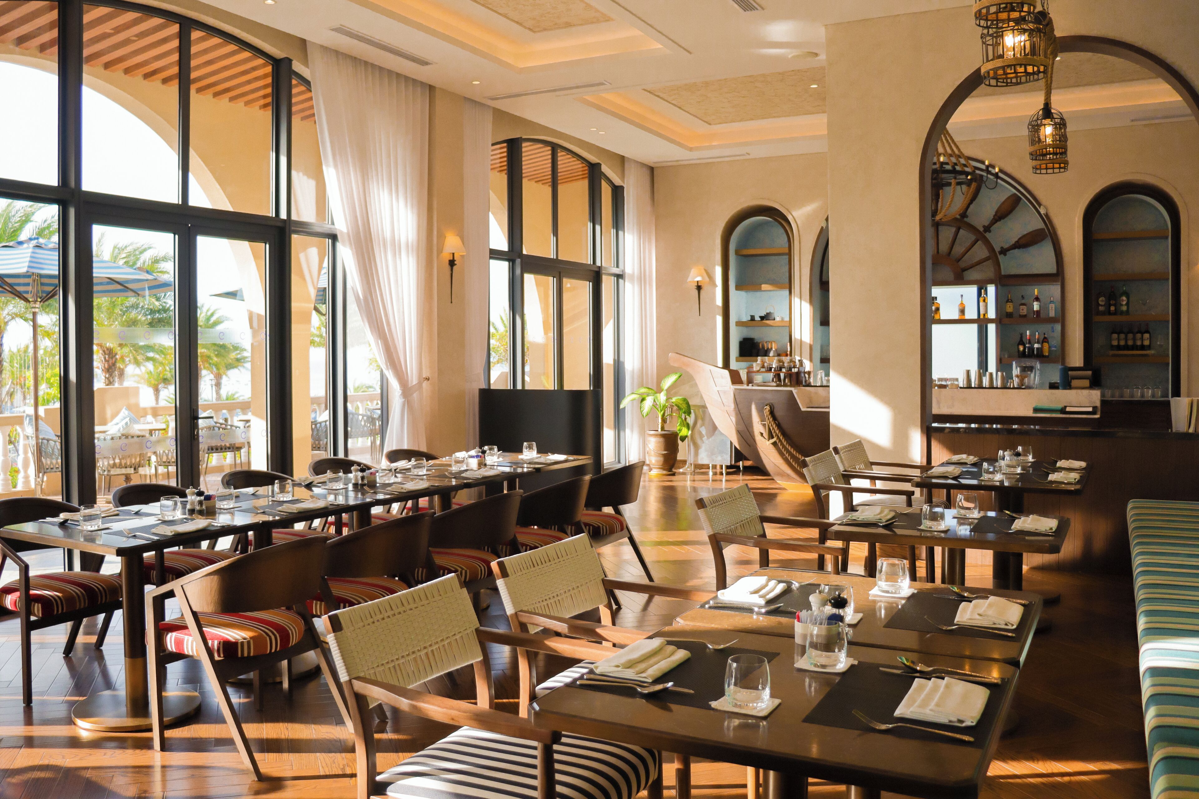 Un comedor amplio con varias mesas y sillas, ventanas grandes y vistas al exterior.