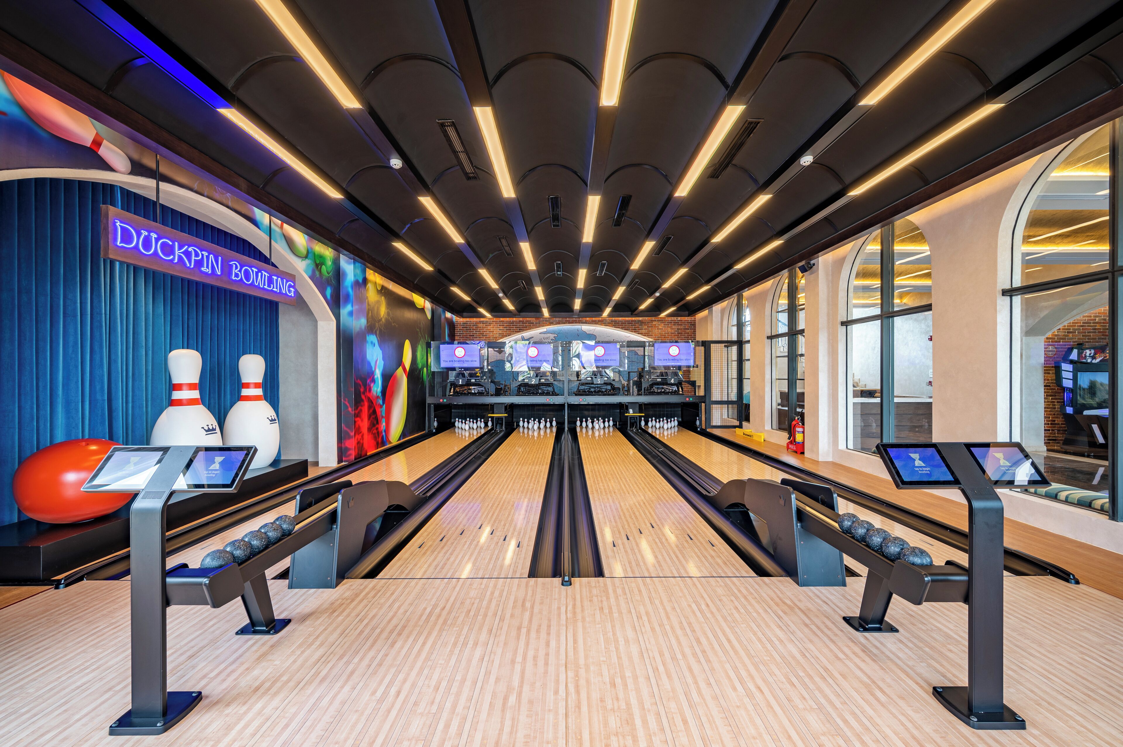 A bowling alley with multiple lanes, a Duckpin bowling sign, and a modern ceiling design.