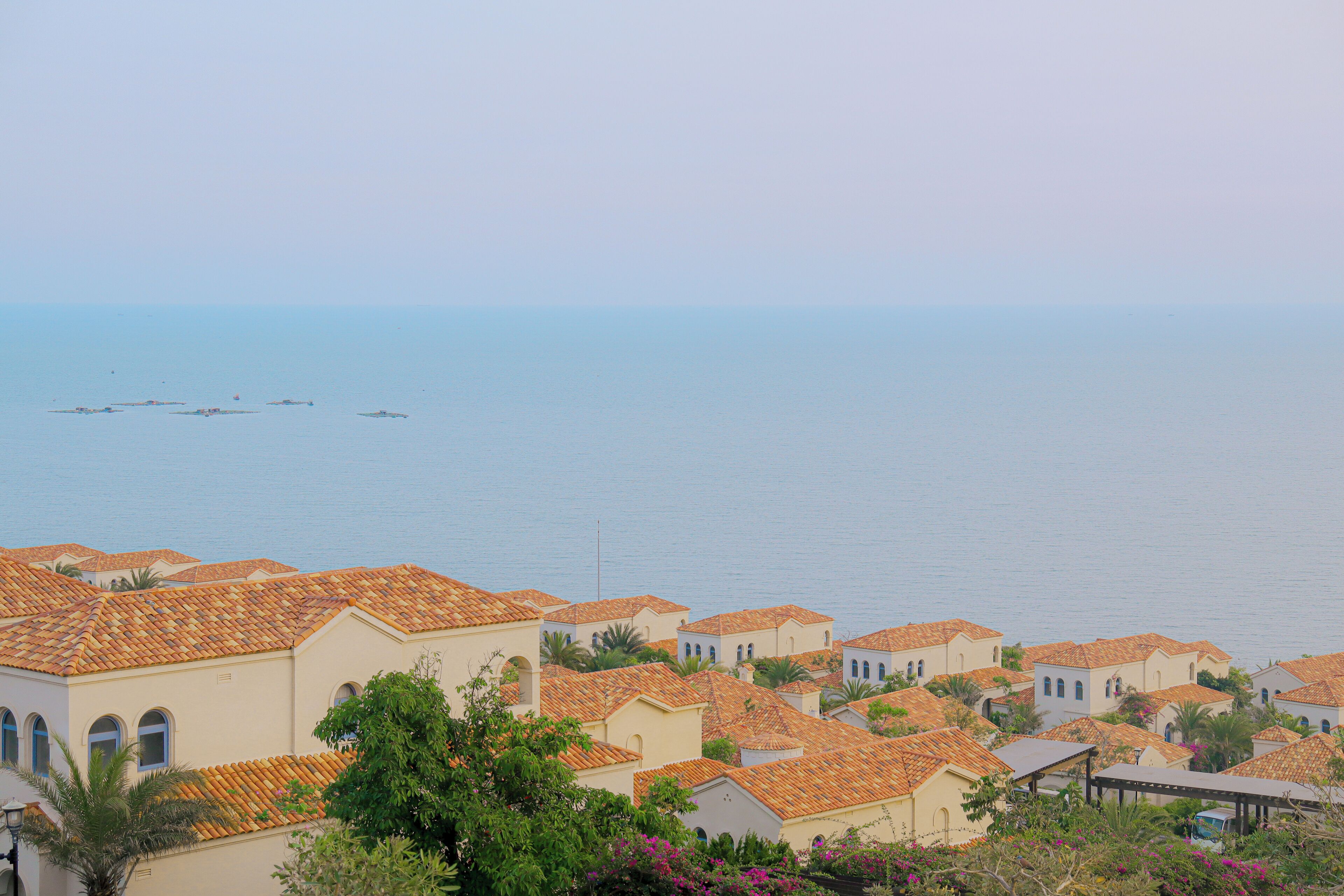 Una zona residenziale costiera con case a tetti in terracotta, alcune con balconi a vista, e una vista libera sul mare.