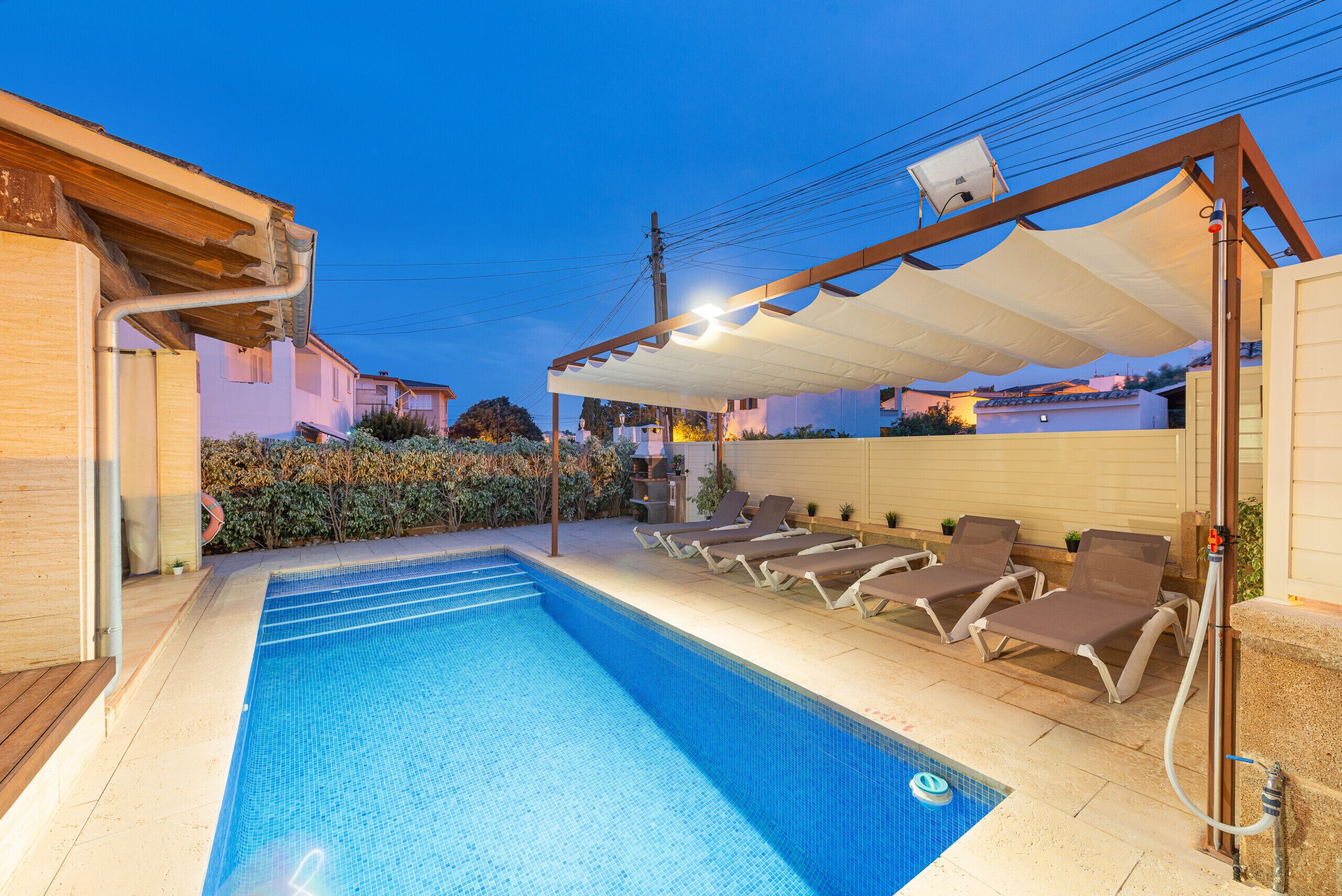 A swimming pool with lounge chairs and a covered area, surrounded by buildings.