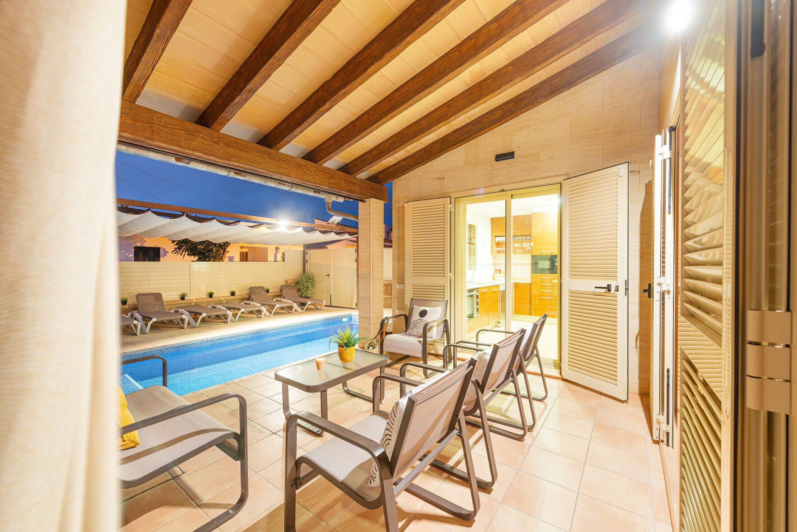 Un espace piscine intérieur avec des chaises longues et une table, des poutres en bois au plafond et une vue sur l’extérieur.