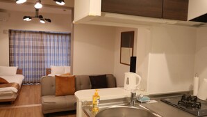 A modern kitchen with a central island, dark cabinetry, and a built-in stove. - Legatio HAKATA (Fukuoka)