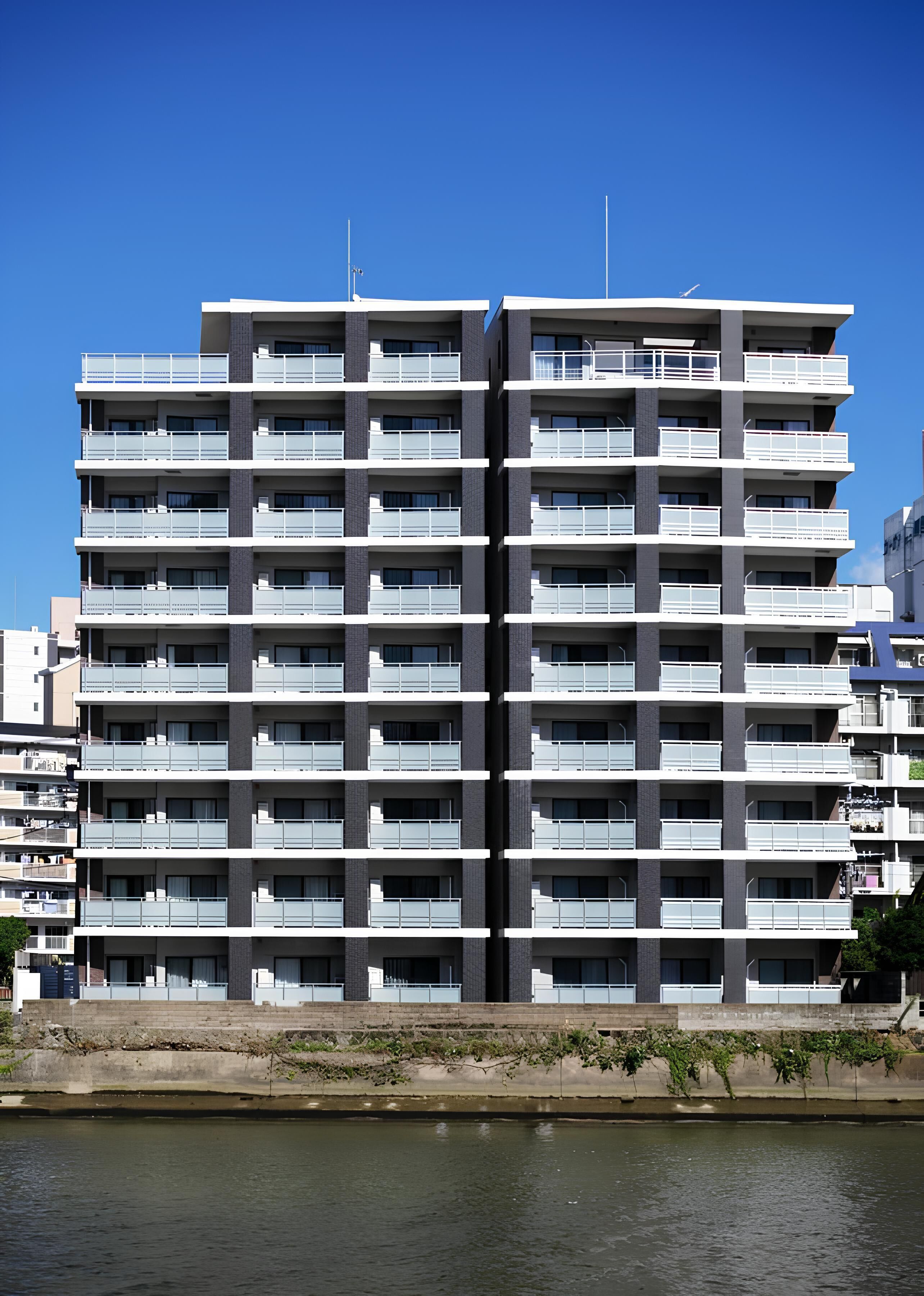 A modern multi-story building with balconies, located beside a body of water.