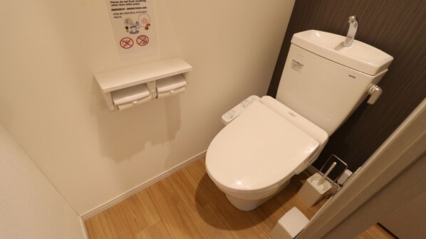 A small, clean bathroom with a toilet, a toilet paper holder, and a wall-mounted sign with instructions.
