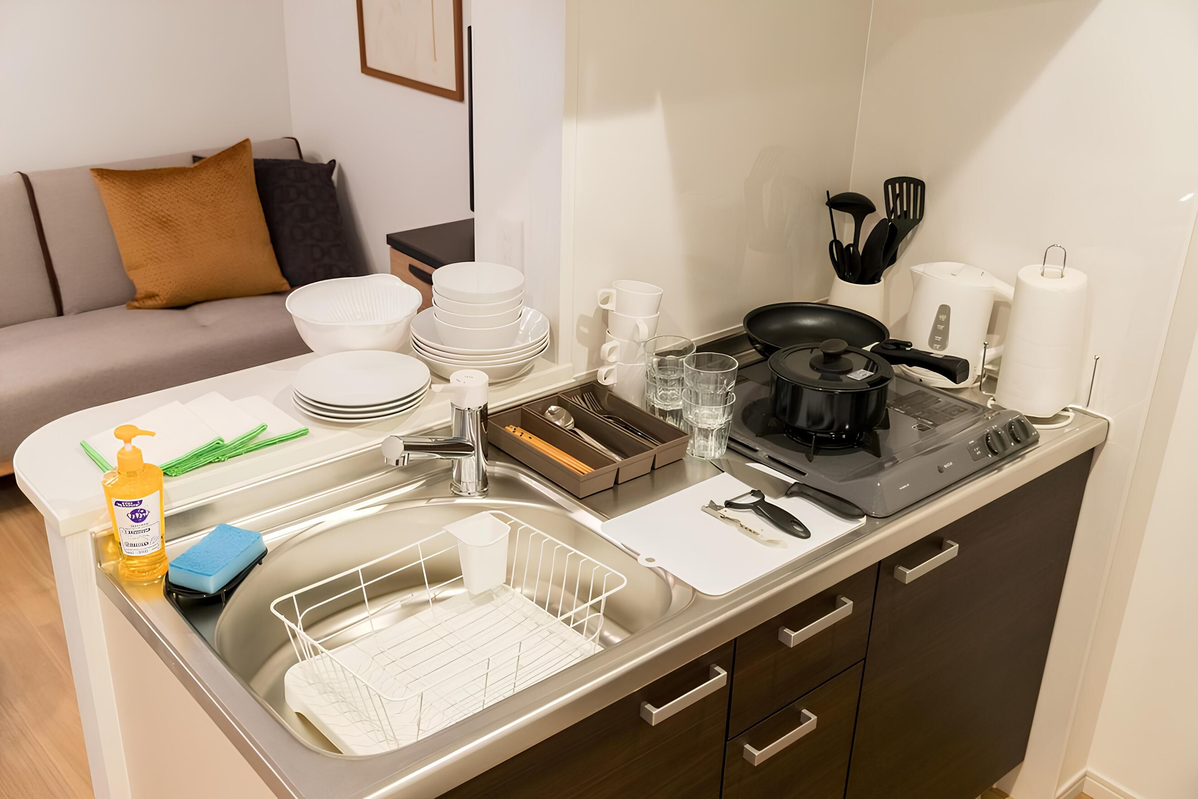 Een kleine keuken met een spoelbak, fornuis en verschillende keukengerei. Er is een zithoek met een bank en kussens.