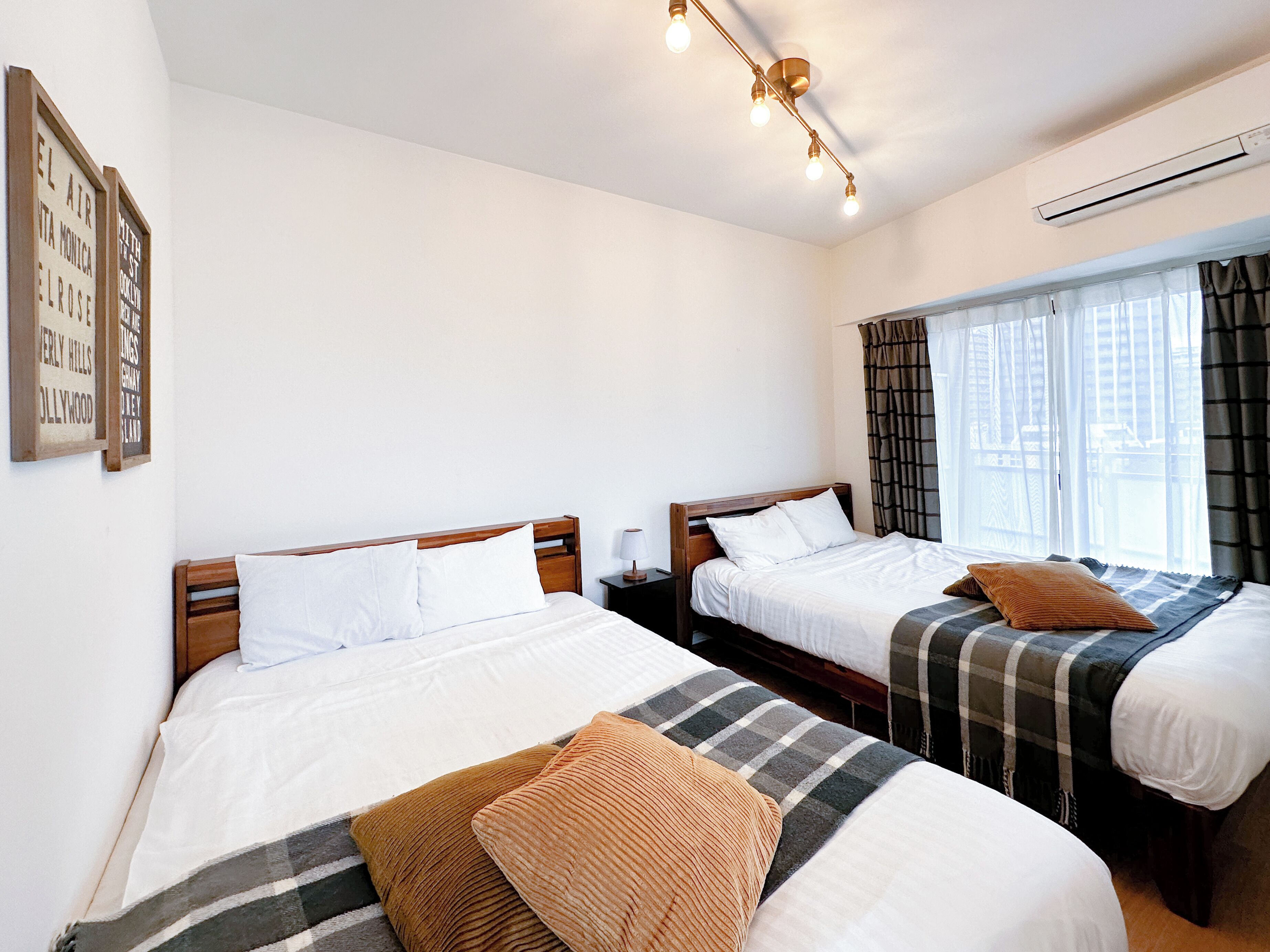 Een hotelkamer met twee bedden, een raam met gordijnen, een wandairconditioner en een plafondlamp.