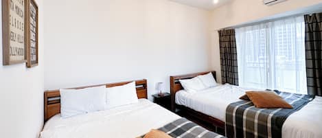 A hotel room with two beds, a window with curtains, a wall-mounted air conditioner, and a ceiling light fixture.