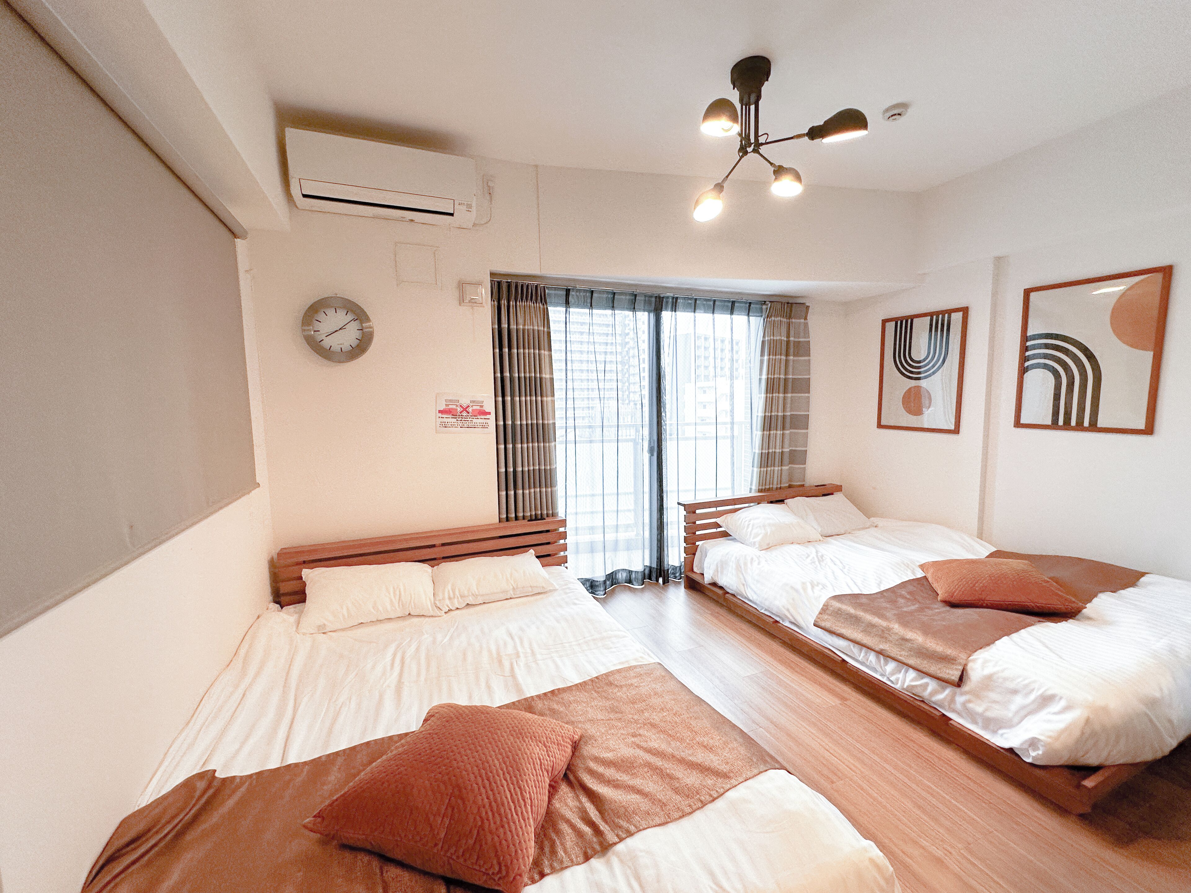 A hotel room with two beds, a ceiling fan, an air conditioning unit, a clock, and a window with curtains.