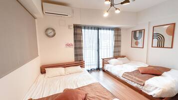A hotel room with two beds, a ceiling fan, an air conditioning unit, a clock, and a window with curtains.