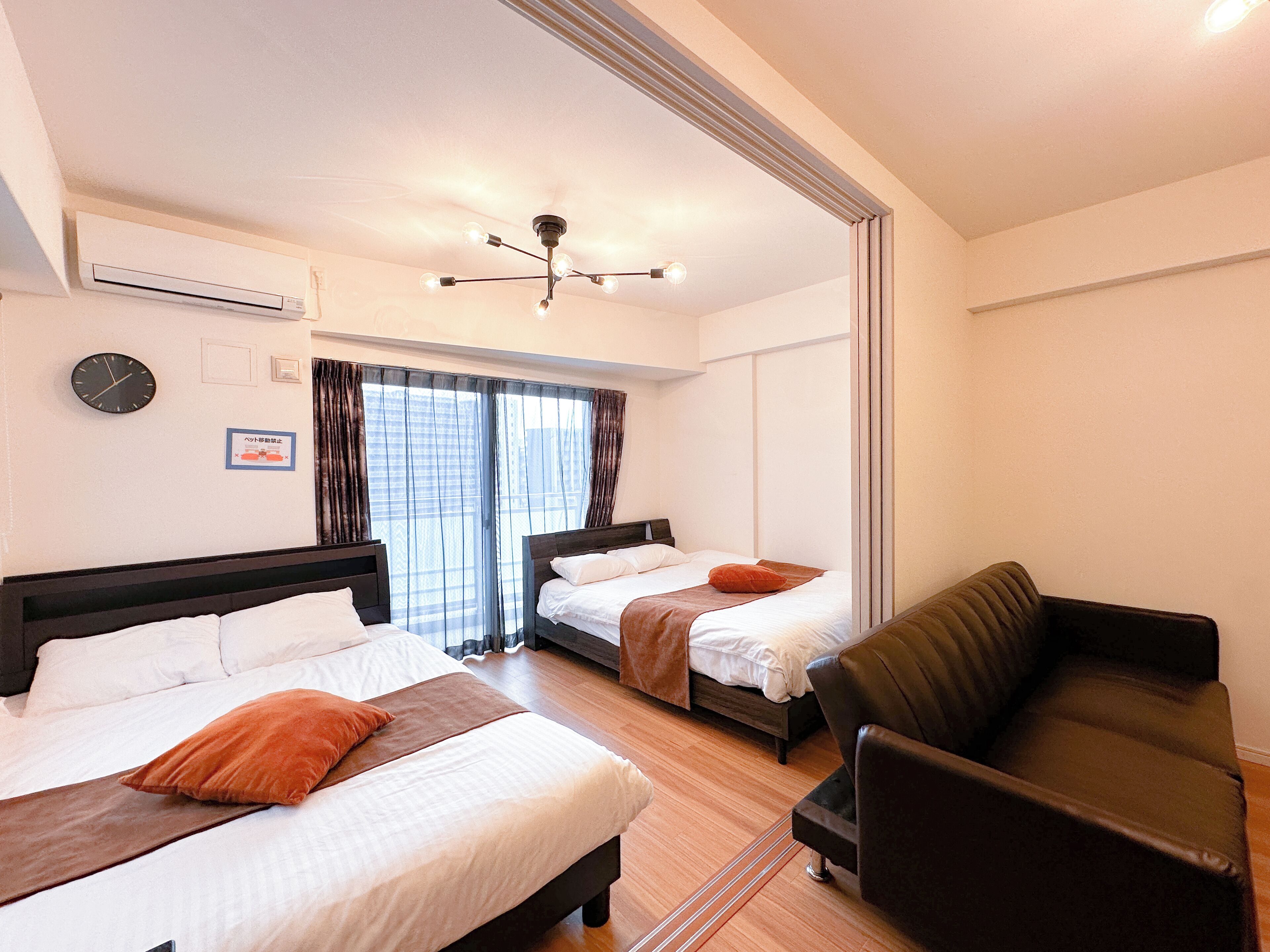 A hotel room with two beds, a sofa, a ceiling fan, and a clock on the wall.