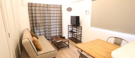 Ein gemütlicher Wohnraum mit einer Couch, einem Couchtisch, einem Fernseher auf einem Schrank und einem Esstisch mit Stühlen.