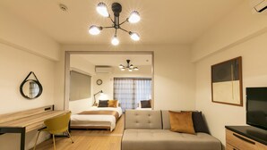 A modern hotel room with a wooden desk, a sofa, a TV, and a ceiling light fixture. - Legatio HAKATA (Fukuoka)