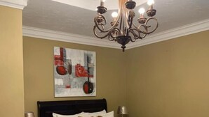 Un dormitorio con una cama grande, una araña, un cuadro en la pared y una alfombra estampada.