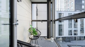 Un balcón moderno con puerta de vidrio, una planta en maceta, una silla negra y un farol transparente.