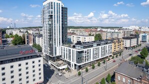 Un área urbana moderna con un edificio alto destacado que presenta fachada de vidrio y un hotel Scandic con techo plano y varios pisos.