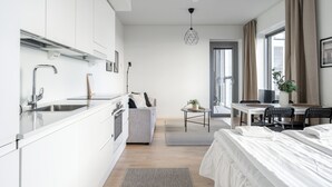 Una cocina moderna con armarios blancos, un sofá gris, una mesa de comedor con sillas y una cama con ropa de cama blanca.