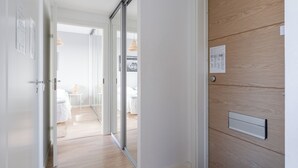Un pasillo con un ventanal corredera que da a un dormitorio con cama y una mesita.