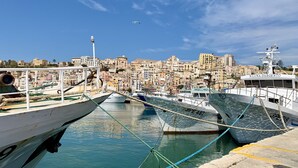 A harbor with boats docked, a cityscape in the background, and a clear sky. - The fisherman's house (Sciacca)