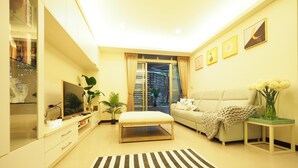 A modern living room with a sofa, a coffee table, a TV, and a large window with curtains.