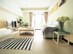 A modern living room with a sofa, a coffee table, a TV, and a decorative vase with flowers.