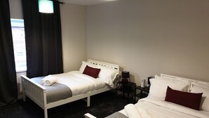 Et hotelværelse med to senge, et natbord med lampe og et vindue med gardiner.