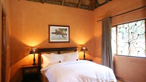 A bedroom with a bed, two bedside tables, a nightstand, a window with curtains, and a framed picture on the wall. - Olievenfontein Private Game Reserve (Vaalwater)