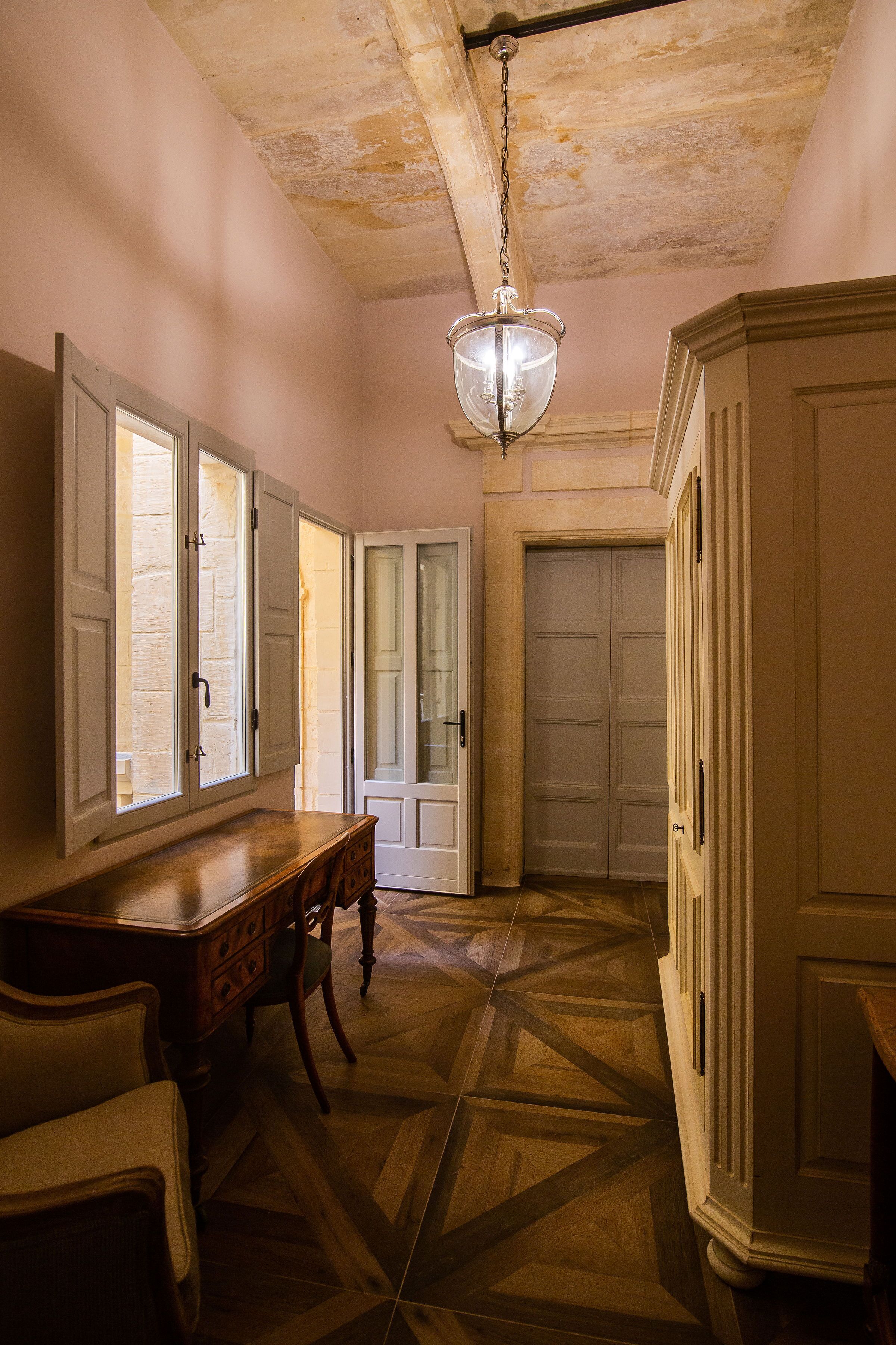 A hallway with a wooden floor, a dining table with chairs, and a chandelier.