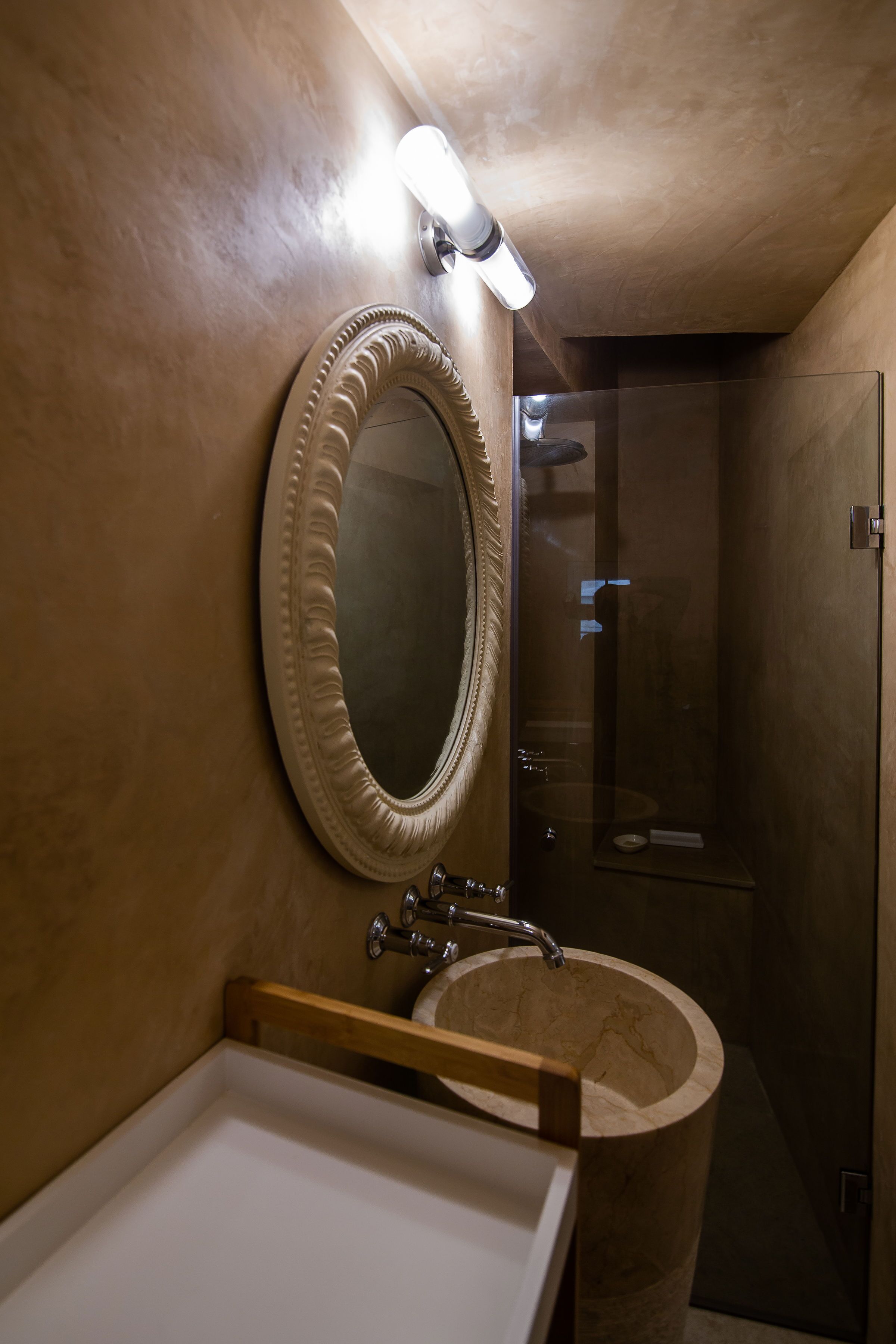 Un baño con un espejo redondo, un lavamanos y una ducha.