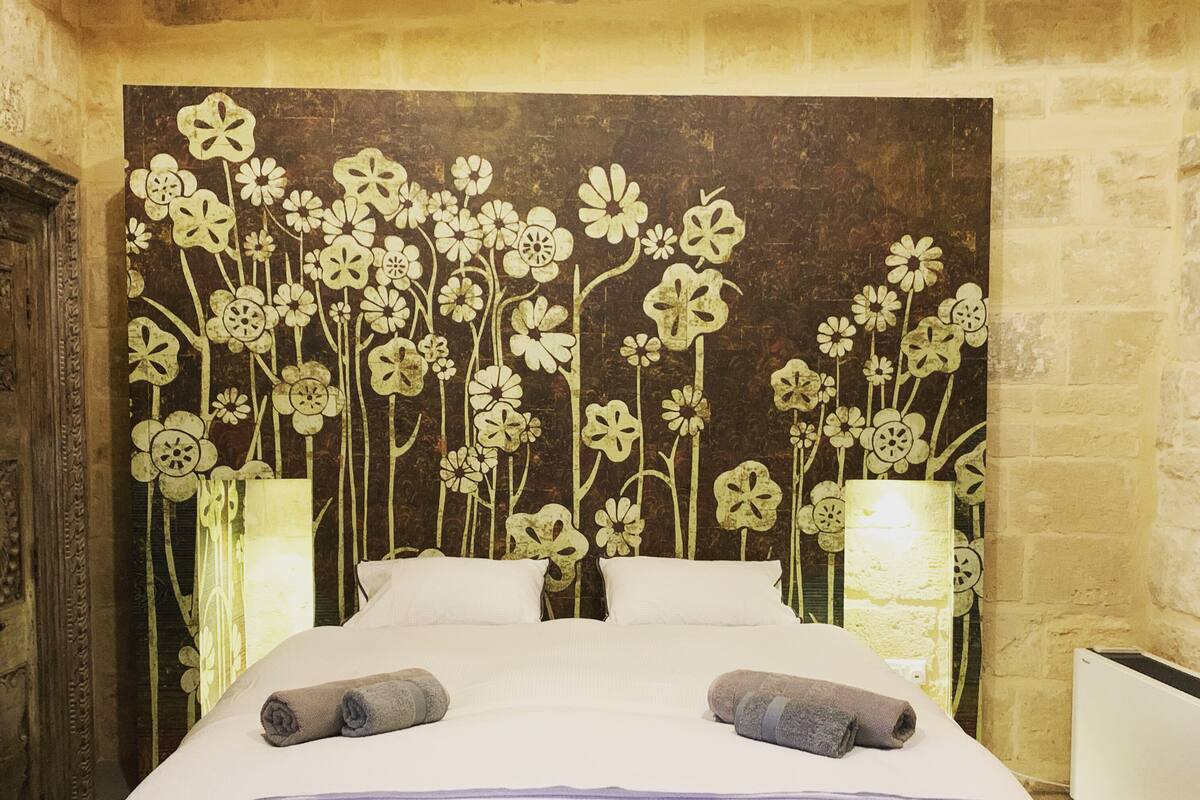 Un dormitorio con una cama grande, dos almohadas, un cabecero tapizado color verde y un mural floral en la pared.