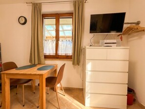 A room with a wooden table, two chairs, a white dresser, a flat-screen TV, and a window with curtains. - Appartamento Petra Piccolo (Tignale)
