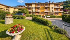 Un immeuble résidentiel à plusieurs étages, doté de balcons, d’une allée pavée et d’un jardin bien entretenu avec des parterres de fleurs.