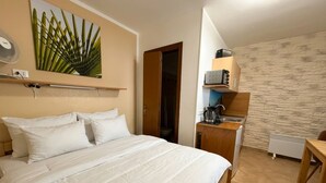 Une chambre avec un lit, une petite kitchenette et une porte donnant sur la salle de bain.