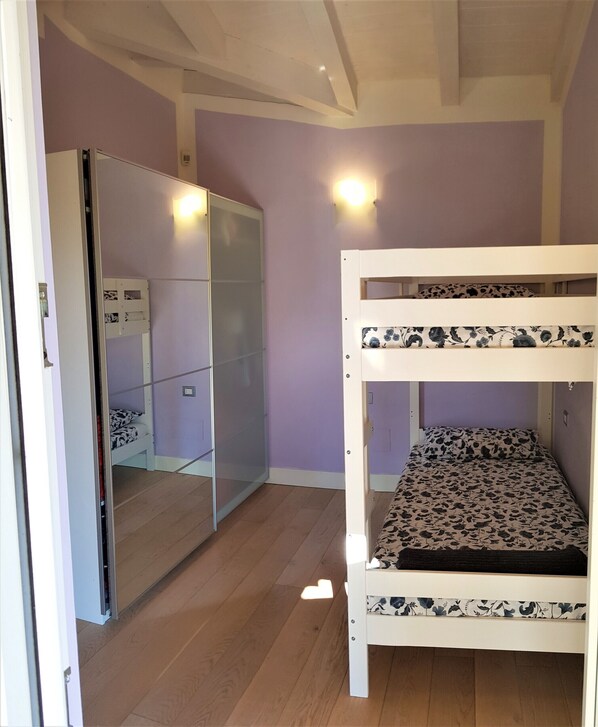 Quarto com beliche, guarda-roupa com espelho e luminária na parede.