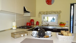 Una cocina con estufa a gas, cafetera roja y ventana con vistas.