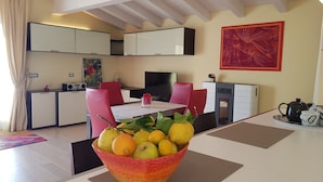 Una cocina moderna con armarios blancos, un comedor con mesa y sillas, y un frutero sobre la mesa.