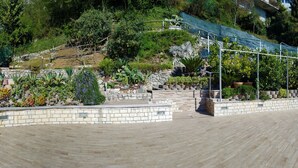 Un jardín ajardinado con muros de piedra, diversas plantas y una terraza de madera.