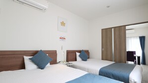 Habitación de hotel con dos camas, una mesita de noche con lámpara, aire acondicionado instalado en la pared y una puerta que da a un balcón con vistas.