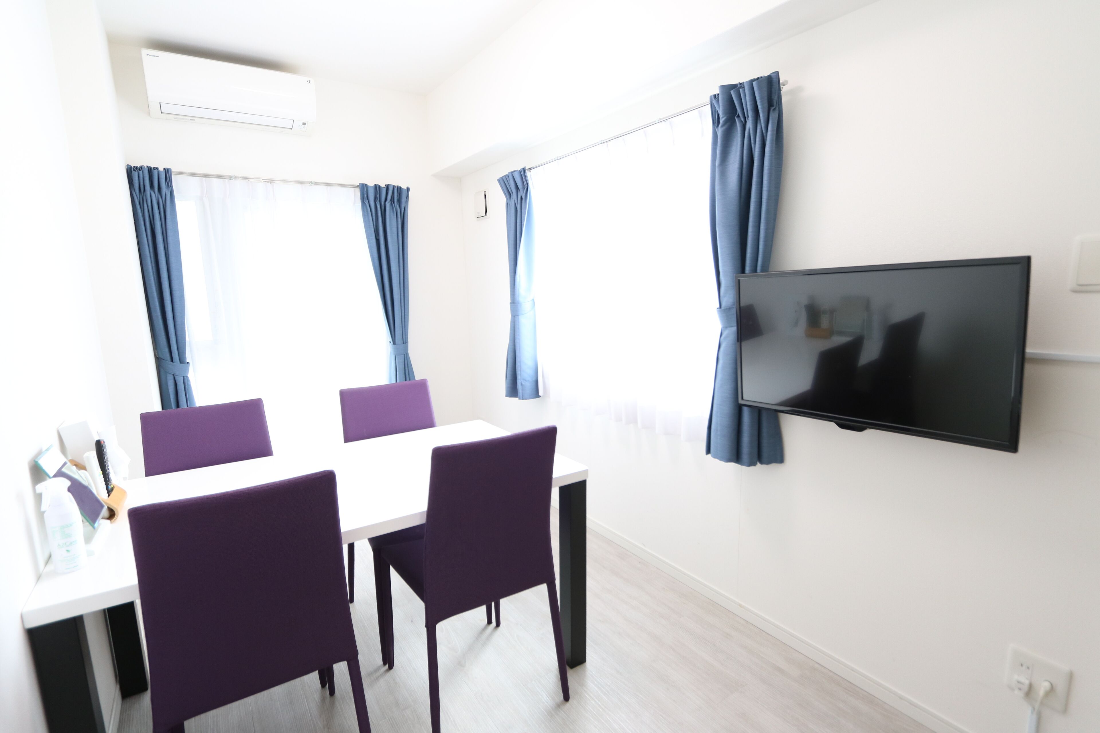 A modern room with a white table, purple chairs, a flat-screen TV, and blue curtains.