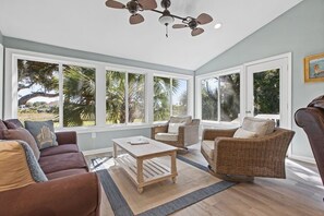 A spacious living area with large windows, a ceiling fan, and a view of palm trees. - 2 BR + Loft/2BA Tarpon Pond Cottage! Great Views! Amenity access included (Seabrook Island)