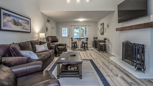 A spacious living room with a leather sofa, a coffee table, and a fireplace. There is a dining area with a table and chairs, and a TV mounted on the wall. - 2 BR + Loft/2BA Tarpon Pond Cottage! Great Views! Amenity access included (Seabrook Island)