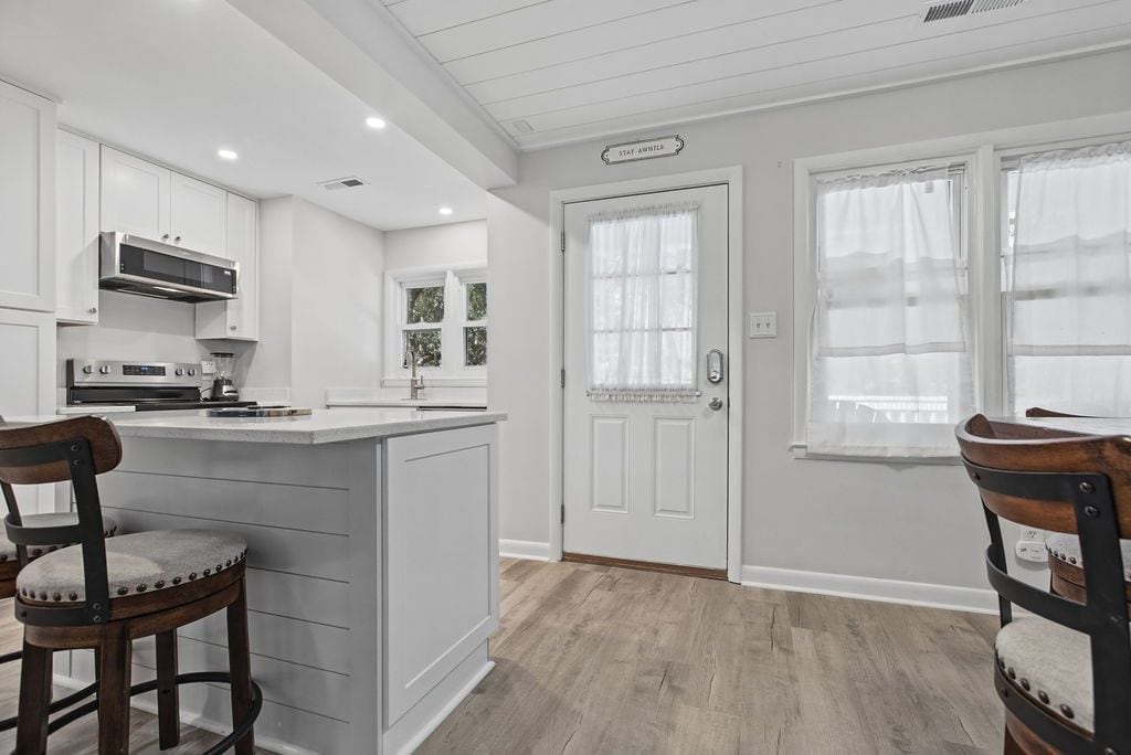 Una cocina con muebles blancos, una isla central y un comedor con dos sillas.