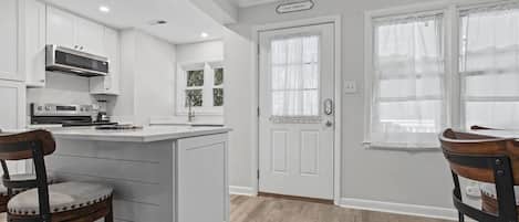 Una cocina con muebles blancos, una isla central y un comedor con dos sillas.