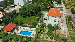 Vista aèria d'una zona residencial amb piscina, un edifici amb teulada vermella i vegetació als voltants.