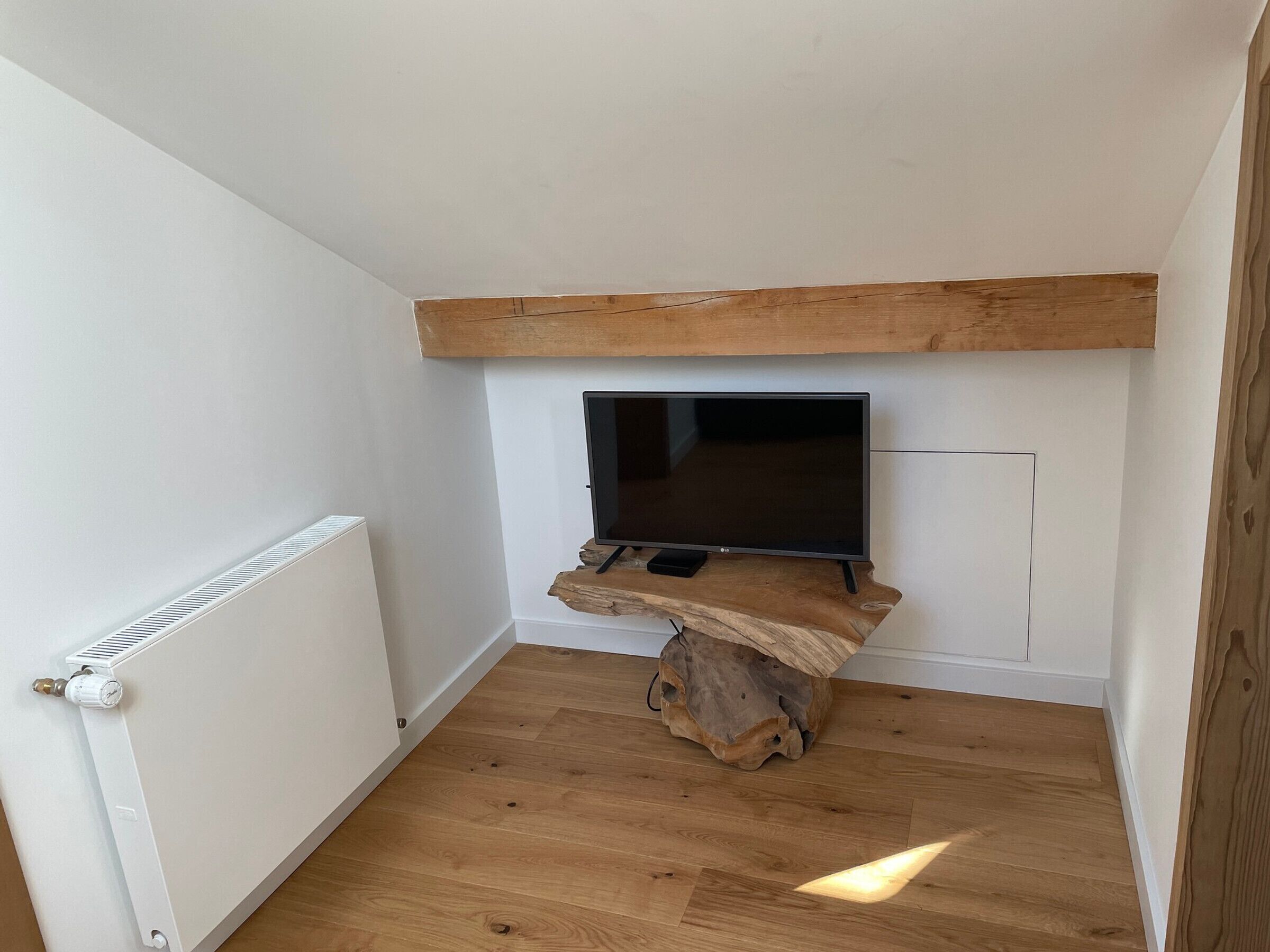 Una habitación de esquina con un mueble de televisión de madera, un radiador y una pared blanca.