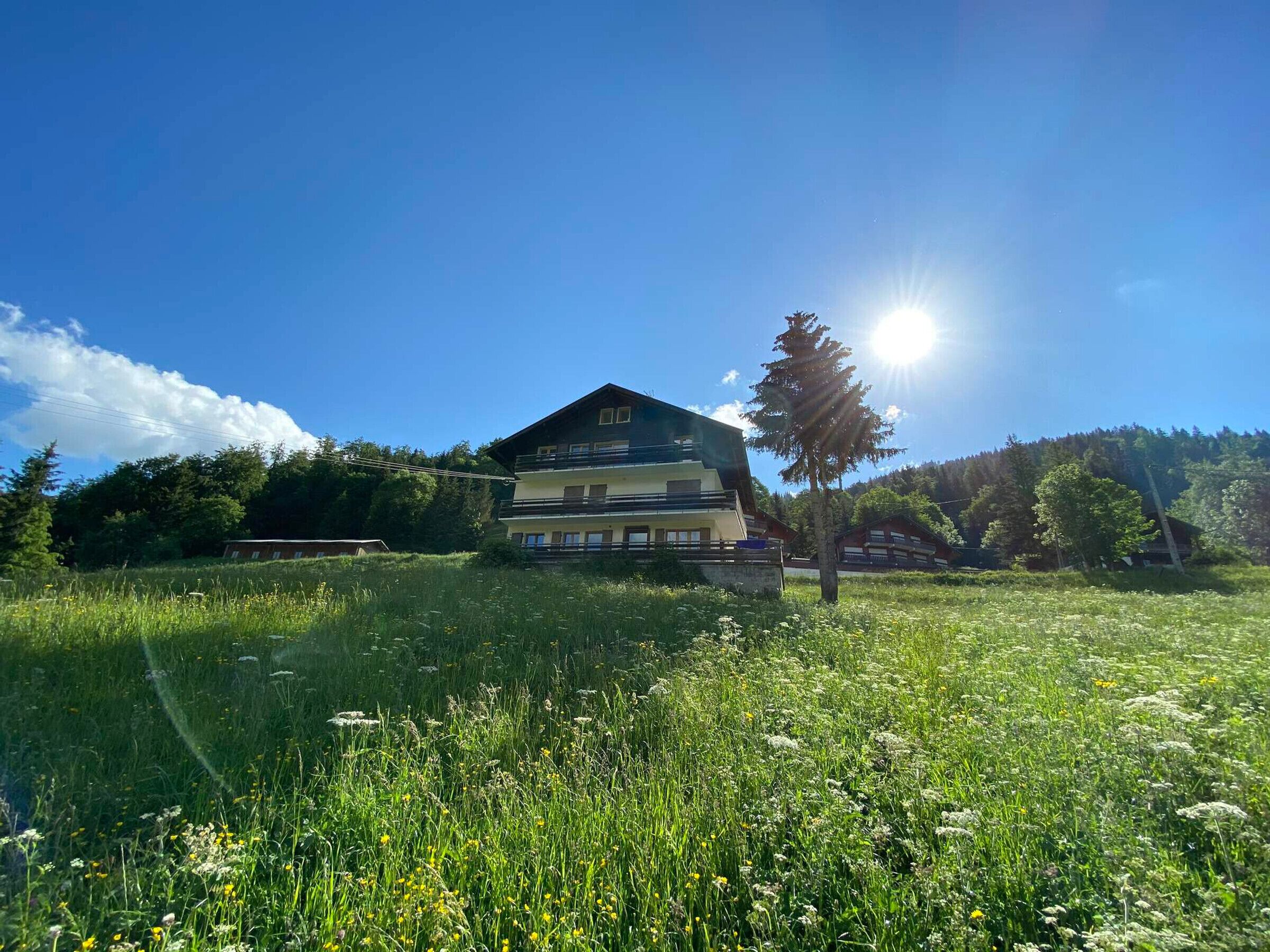 A two-story building with balconies, surrounded by a grassy field and trees, under a clear blue sky.